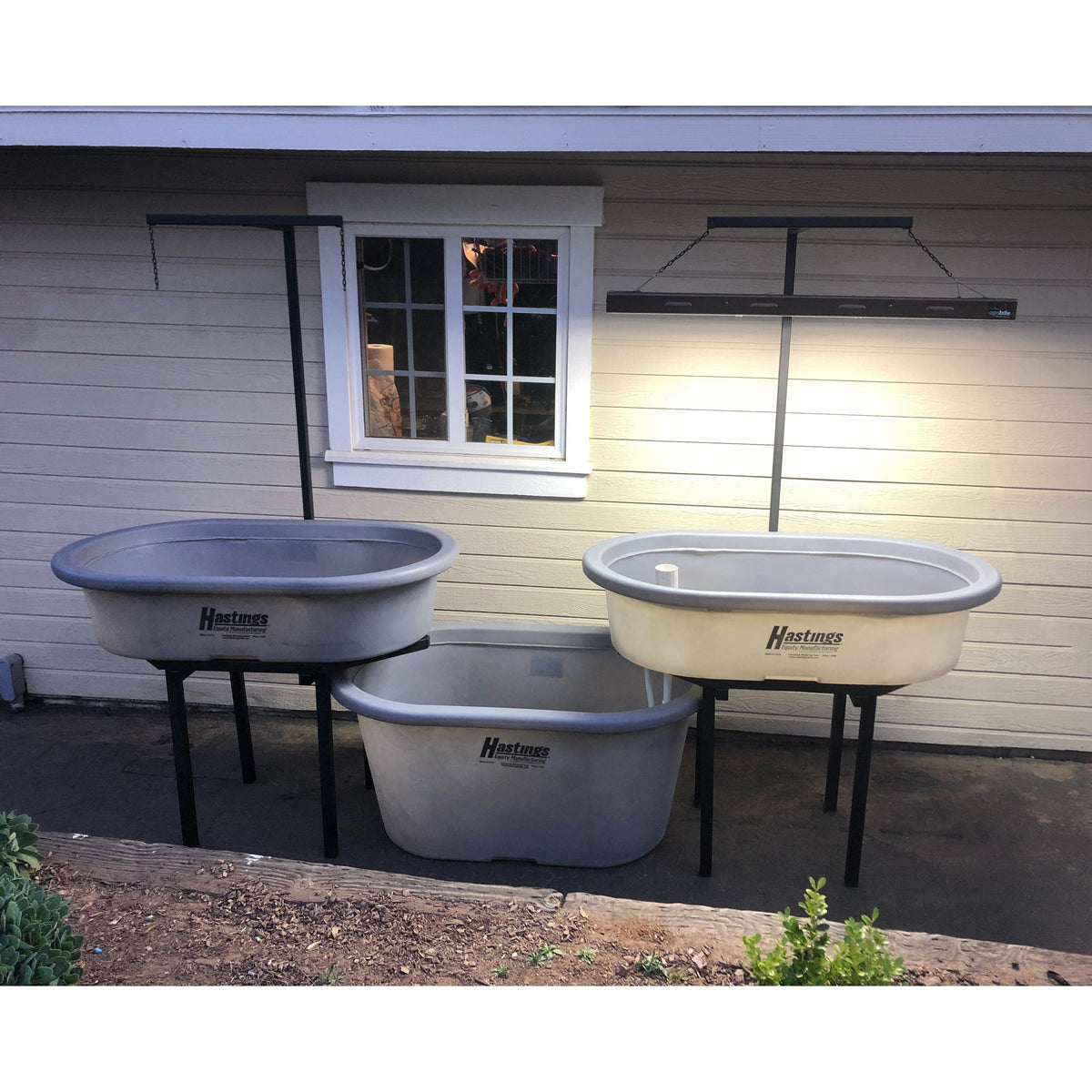 A Go Green Double Aquaponics System featuring three gray tubs on a stand outside of a house.