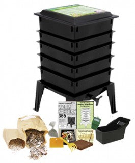 The Natures Footprint Worm Factory 365 Vermicomposting System, in black with multiple tiers and legs, comes with a starter kit including paper scraps, a handbook, a small bin, and composting tools displayed in front.
