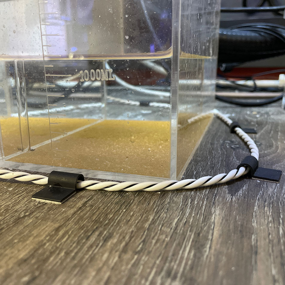 A plastic container with a small amount of water in it, equipped with a TAS HYDROS Rope Leak Detection Extension Cable for monitoring and an extension cable.