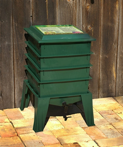 A green Worm Factory 365 Vermicomposting System by Natures Footprint sitting on a brick floor.